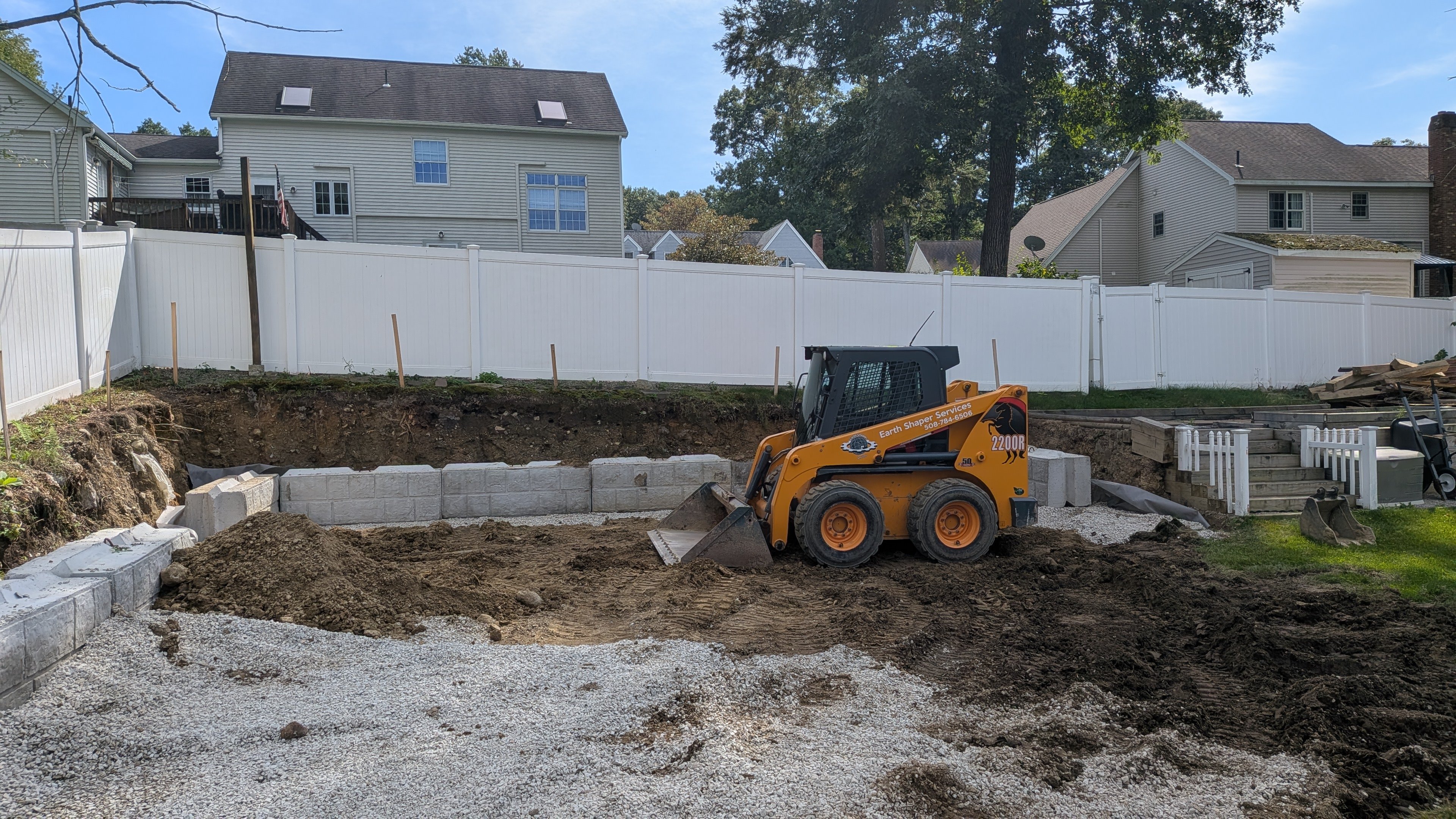 Earth Shaper Services skid steer grading beside a new block retaining wall